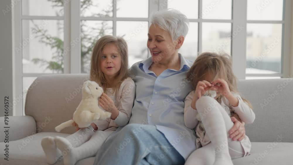 Grandmother with granddaughters resting. Happy relaxed older adult granny embracing playing with toys with children twins grandchildren leisure rest on couch at home. Mothers love, generation concept. Grandmother with granddaughters resting. Happy relaxed older adult granny embracing playing with toys with children twins grandchildren leisure rest on couch at home. Mothers love, generation concept.