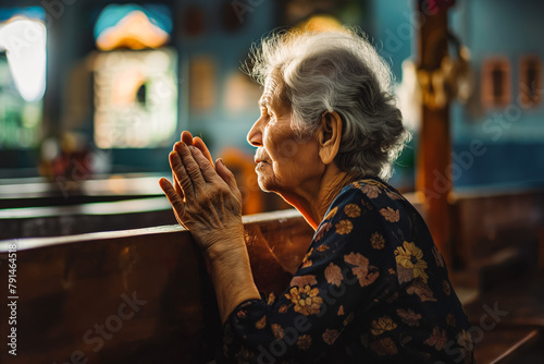 Elderly woman sitting on the bench in small church and praying photo