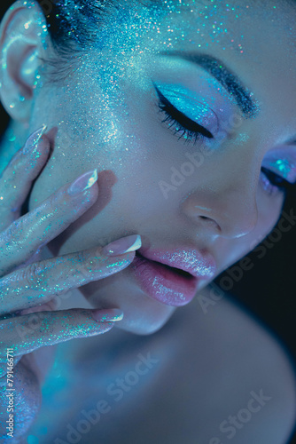 Woman cosmic themed glitter beauty makeup, highlighting eyes and cheeks under blue lighting