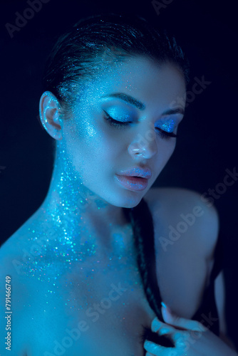 Woman wearing striking blue beauty makeup with glitter applied on her body