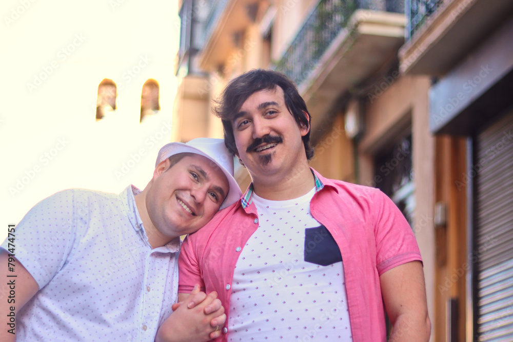 Fototapeta premium Couple of gay men arm in arm smiling walking down the street, one rests his head on the other, outdoor, normal people. LGBT couple concept