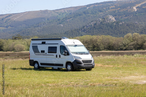 A modern white camper van is parked on a grassy field with hills and wind turbines in the background, perfect for illustrating road trip adventures