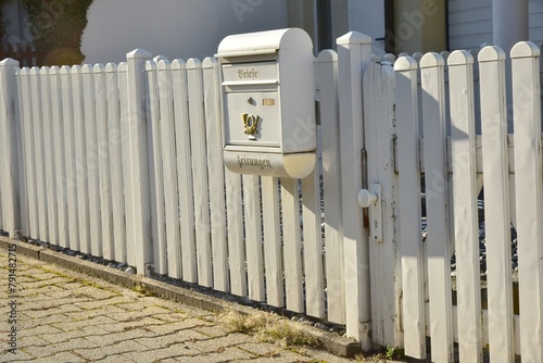 Weiß lackierter Lattenzaun um einen Vorgarten mit nostalgischem Briefkasten