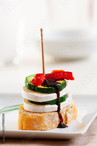 Pintxo or Basque pincho. Delicious Spanish tapa with slice of goat cheese with zucchini and red pepper...