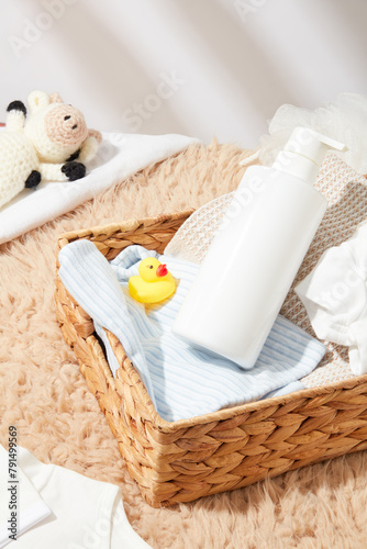 Template for baby bath accessories advertising, a rattan basket contains products for baby bath, a rubber duck, a blue striped towel and a blank label bottle. Top view photo, copy space