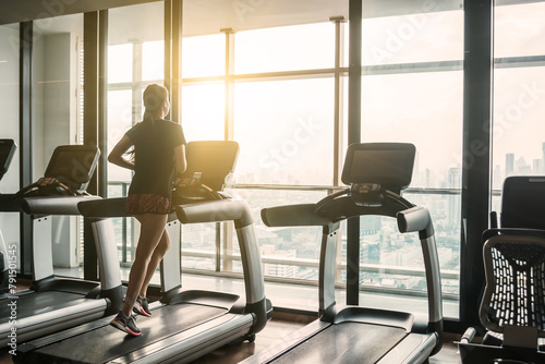 A focused young woman jogging on a treadmill at a high-rise gym with a panoramic urban view.