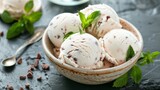 A bowl filled with scoops of creamy mint chocolate chip ice cream on a table.