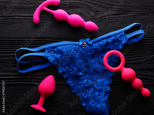 anal plugs and dildo in different shades of pink over black wooden background and blue panty