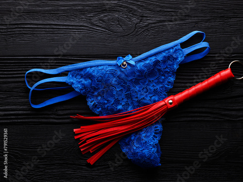 Red whip and blue panty for adult role play games over black wooden background