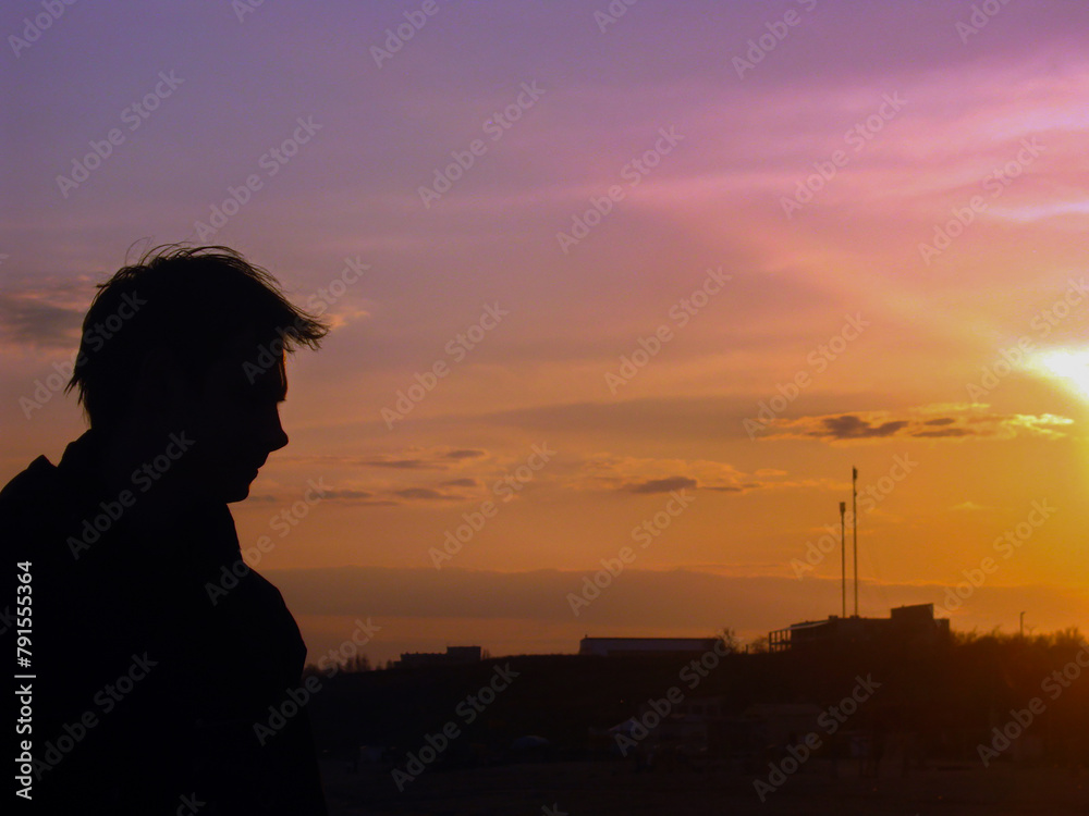 Silhouette of a guy standing on a sea stone against the backdrop of a sunset close up