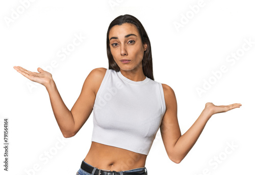 Hispanic young woman doubting and shrugging shoulders in questioning gesture.