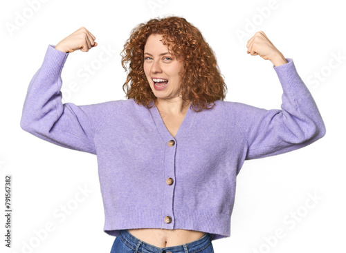 Young Caucasian redhead woman showing strength gesture with arms, symbol of feminine power