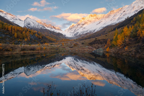 Autumn landscape view of the snow-capped Lotschental mountains reflecting in the Grundsee in Blatten