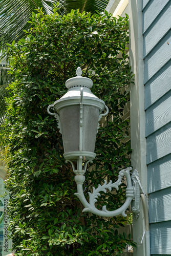 In the courtyard of a condominium, a white decorative lantern hangs on the side of the building. At night the electricity is turned on and it illuminates the area.