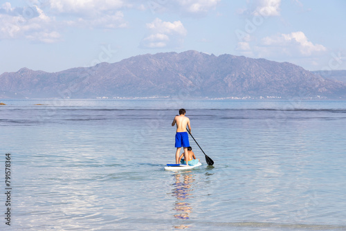 A lone man enjoys paddleboarding on the tranquil blue waters with a mountainous backdrop, reflecting serenity and the simplicity of nature