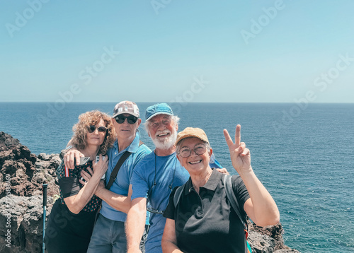 Cheerful group of people in outdoor excursion at sea, four men and women looking smiling at camera enjoying freedom and vacation, positive and healthy activity