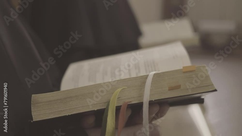 Prayers reading Bible in church, book close up selective focus. Christian monks praying liturgy and holding psalmbook in hands close view with blurred background. Liturgy of the Hours concept
