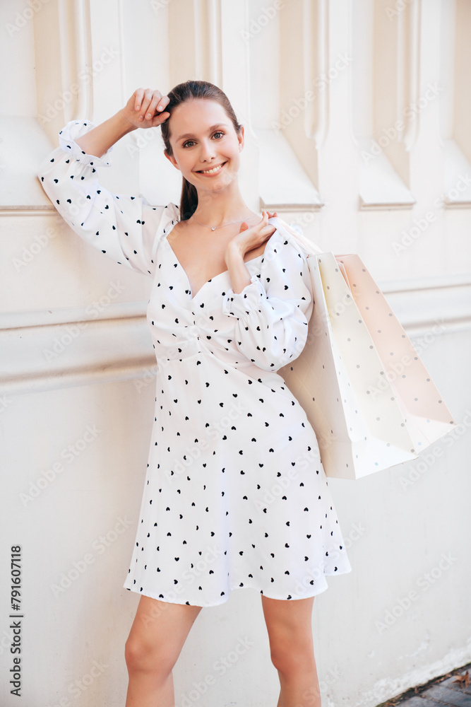 Young beautiful smiling hipster woman in trendy summer clothes. Sexy carefree model walking in the street background at sunset. Positive female holding shopping bag. Posing outdoors Young beautiful smiling hipster woman in trendy summer clothes. Sexy carefree model walking in the street background at sunset. Positive female holding shopping bag. Posing outdoors