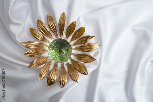 Golden sun flower with green glitter middle on white satin canvas texture, abstract product presentation backdrop
