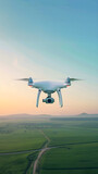 High-Tech White Drone Hovering over Lush Green Field against a Clear Blue Sky Dressed in a Golden Sunset