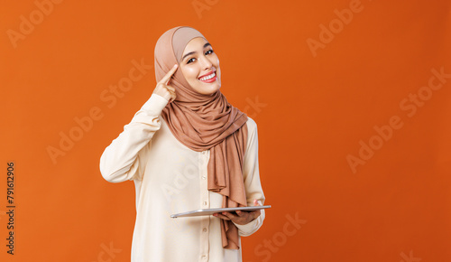 Beautiful smart young smiling muslim woman in traditional religious hijab  reading great news on tablet.