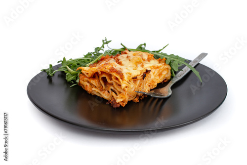 Square slice of lasagna on a black ceramic plate with arugula salad, soft focus close up isolated on white background © Dorin