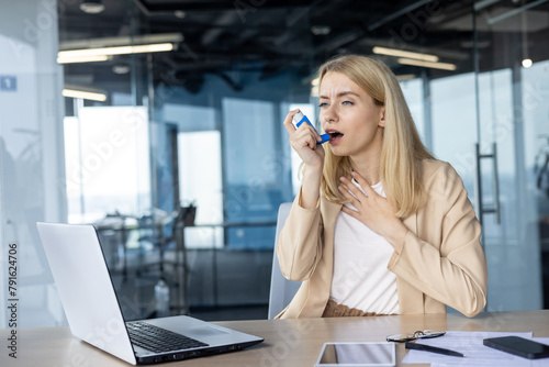 Businesswoman using inhaler during asthma attack in office photo