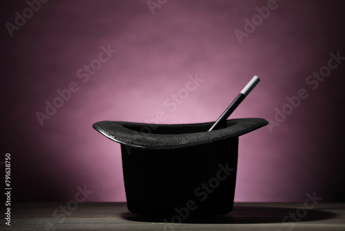 Magician's hat and wand on wooden table against dark background