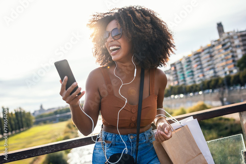 Happy young woman having video conversation with smartphone while staying in the street.