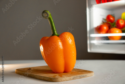 Orange sweet juicy pepper on wooden board on fridge background with food