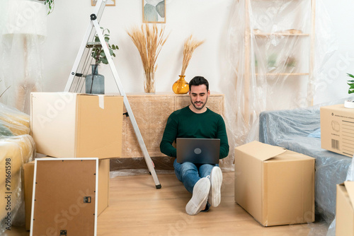 Man with laptop sitting on floor among moving boxes. photo