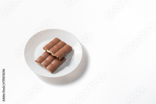 A bar of milk chocolate is broken on a white plate. Milk chocolate on a white background. Chocolate bar broken into pieces on white plate