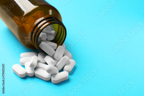 Bottle and vitamin capsules on light blue background, closeup. Space for text