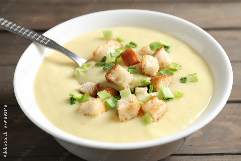 Tasty potato soup with croutons and spoon in bowl on wooden table, closeup