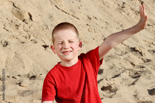 A short-haired six-year-old boy squints and covers the sun with his hand.