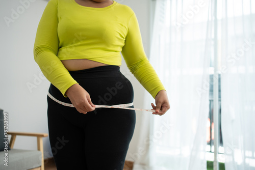 Overweight woman using a tape measure around waist and belly fat, Fat Asian woman workout at home. Concept of healthy, food for health and lifestyle, weight loss