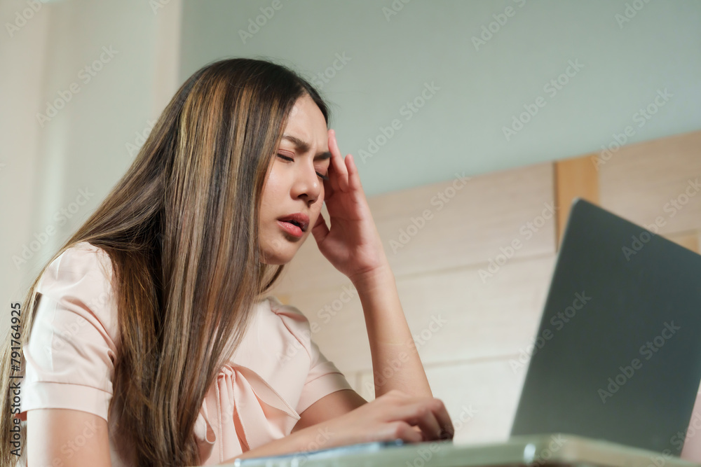 Concerned Asian female in pink attire, pressing temples, stressed or frustrated by laptop screen, wooden backdrop, representing challenges of work or study from home... Concerned Asian female in pink attire, pressing temples, stressed or frustrated by laptop screen, wooden backdrop, representing challenges of work or study from home...