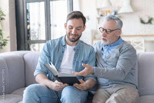 Young loving adult son discussing a novel, new book he read with his elderly old senior father. Family time, togetherness. Happy father`s day! I love you, dad! photo