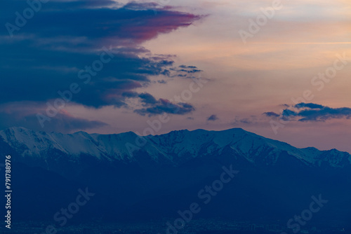 Snow-capped peaks tower over a city as twilight paints the sky in hues of purple and pink.