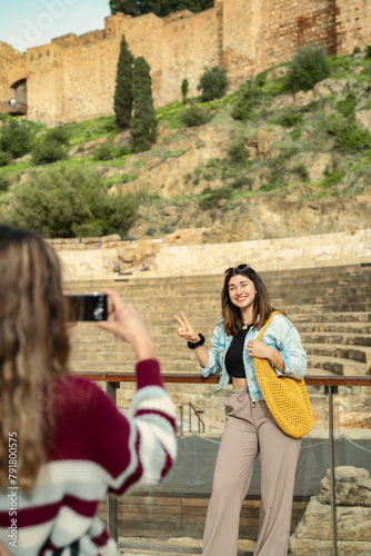 A girl, a tourist, with her back to the camera, joyfully captures her friend as she poses in front of a monument.