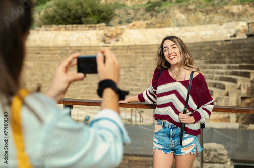 Two tourist friends pose in front of a monument in Malaga while one photographs the other.