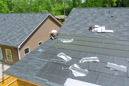 Using an air nail gun, professional roofing contractors install new asphalt bitumen shingles on roof house