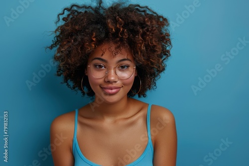 Confident Young Woman With Curly Hair and Glasses on Blue Background