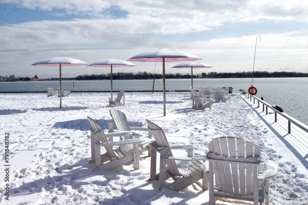 Fototapeta premium pink umbrellas and white Adirondak chairs at a waterfront park covered in snow in winter