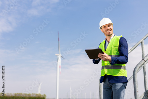 Smiling Engineer With Tablet Inspecting Wind Turbines On A Sunny Day