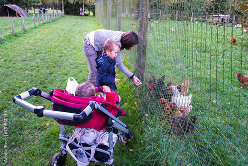 en famille à la ferme, enfants et leur mère nourrissant des poules à la campagne