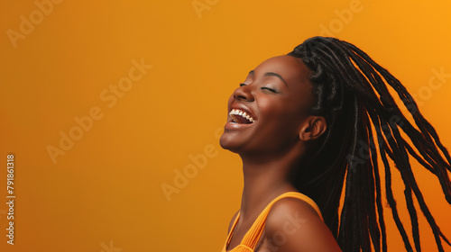 A radiant young woman with braided hair laughs wholeheartedly against a warm orange backdrop, radiating happiness and positivity. photo