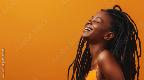 A radiant young woman with braided hair laughs wholeheartedly against a warm orange backdrop, radiating happiness and positivity. photo