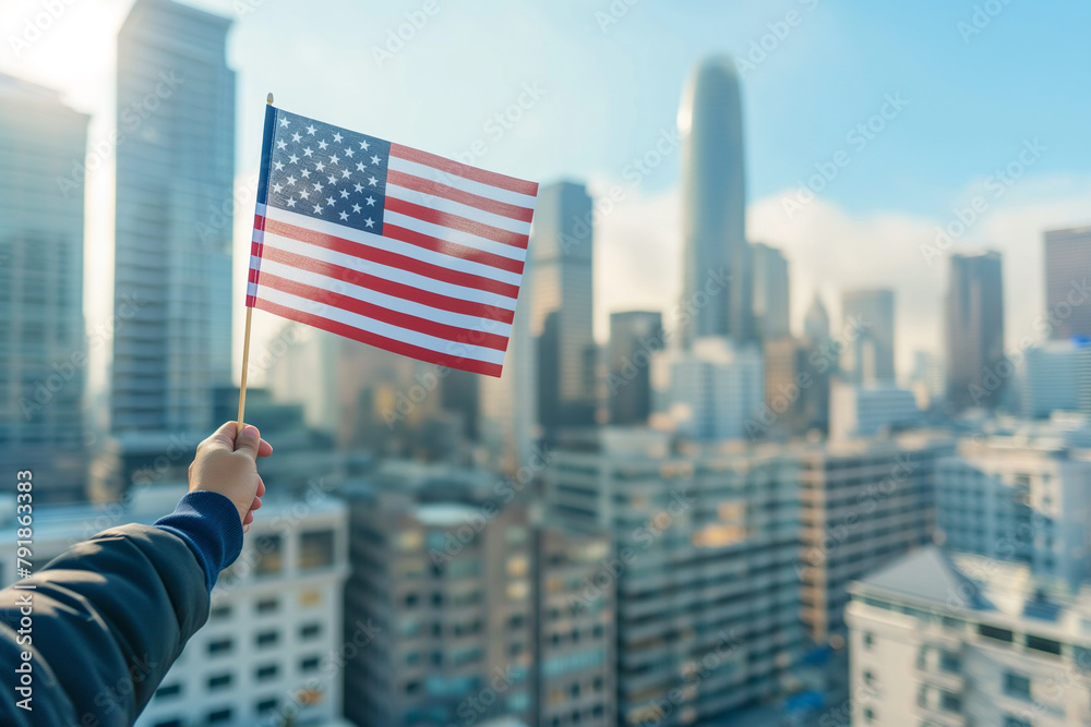 Hand proudly holds the American flag against a sunrise city skyline, conveying a message of patriotism and hope in an urban setting.