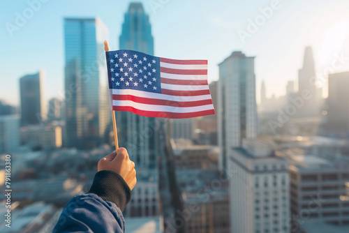 Hand proudly holds the American flag against a sunrise city skyline  conveying a message of patriotism and hope in an urban setting.